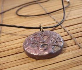 Polymer clay pendant in a circle shape on a leather cord thong, mica powder decoration.